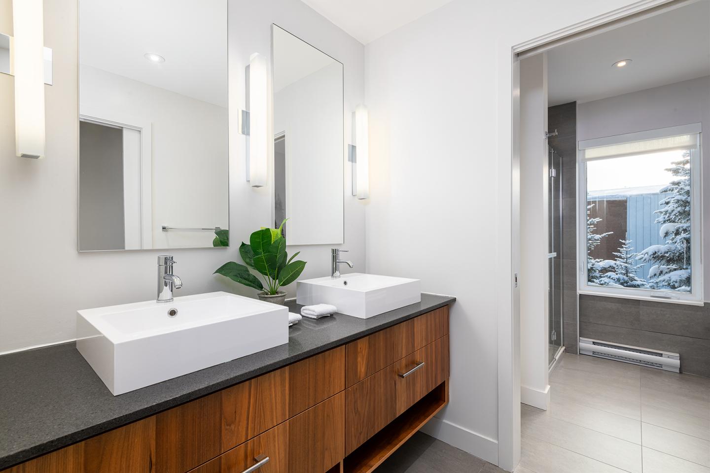 Salle de bain moderne avec deux éviers, miroir large et vue sur l'extérieur.