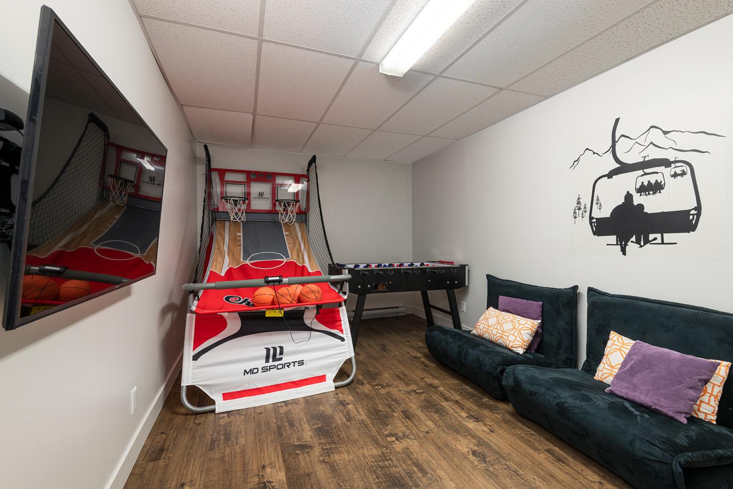 Salle de jeux avec panier de basket, baby-foot, canapé et décoration murale.
