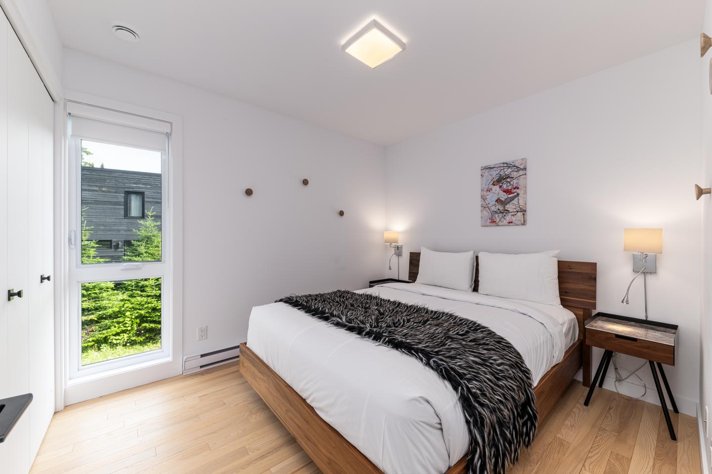 Chambre moderne avec lit double, murs blancs, bois clair, lumière naturelle.