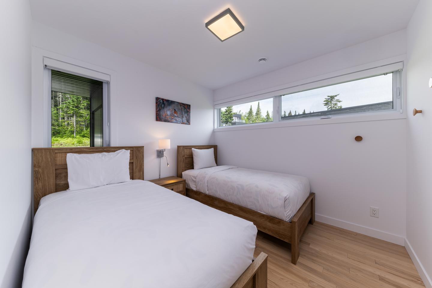 Chambre lumineuse avec deux lits simples, grandes fenêtres et parquet.