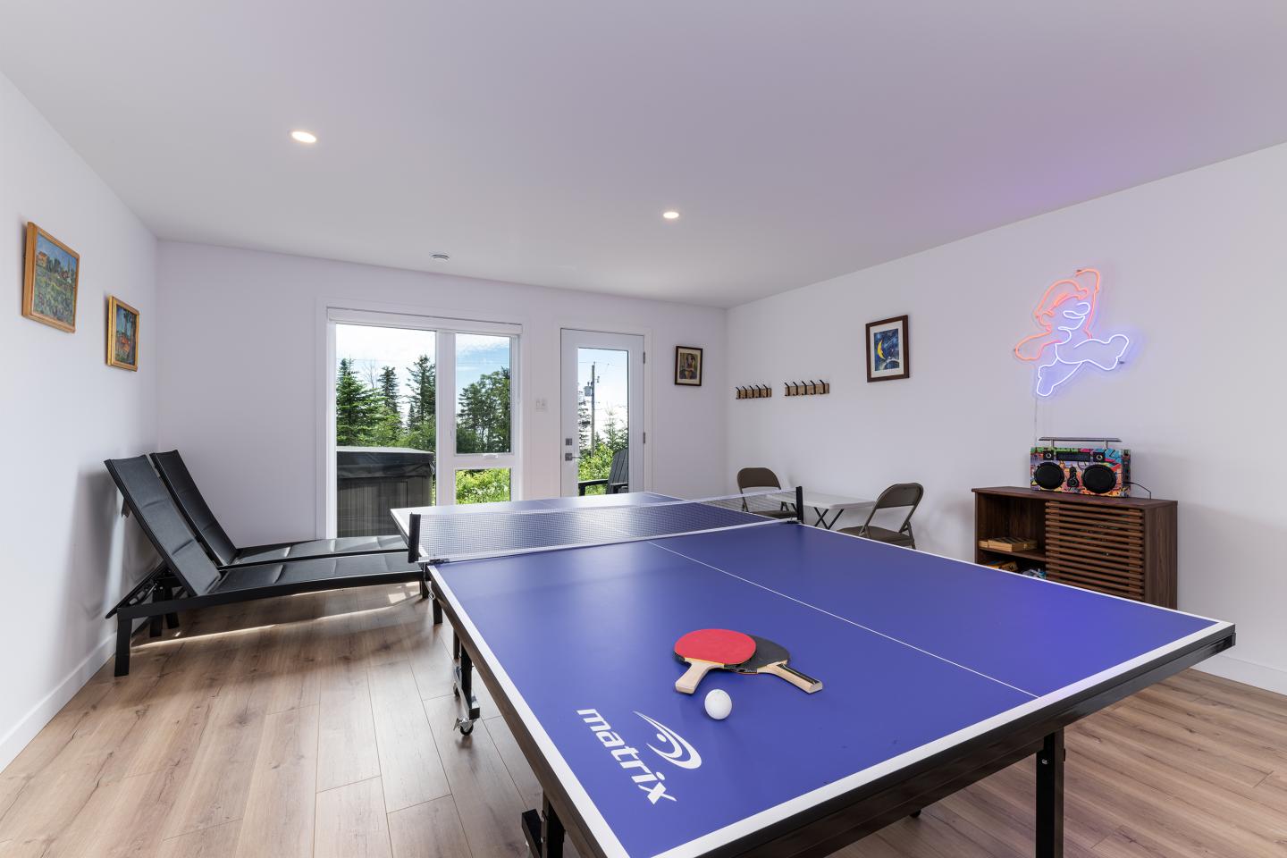Salle de ping-pong avec table bleue, raquette rouge et chaise longue.