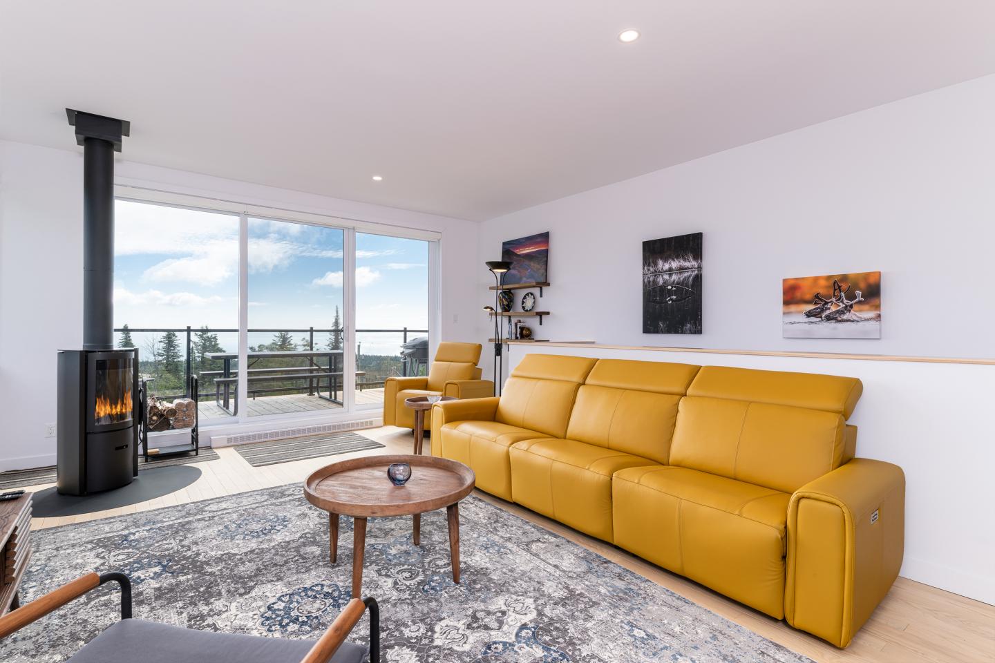 Salon moderne avec canapé jaune, poêle à bois et vue panoramique.