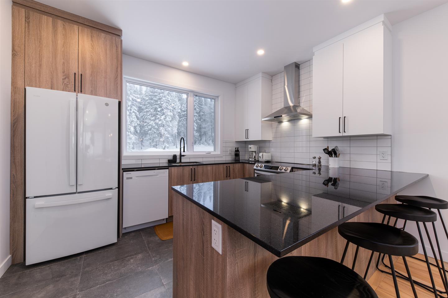 Cuisine moderne avec îlot en marbre noir, chaises et appareils en acier inoxydable.