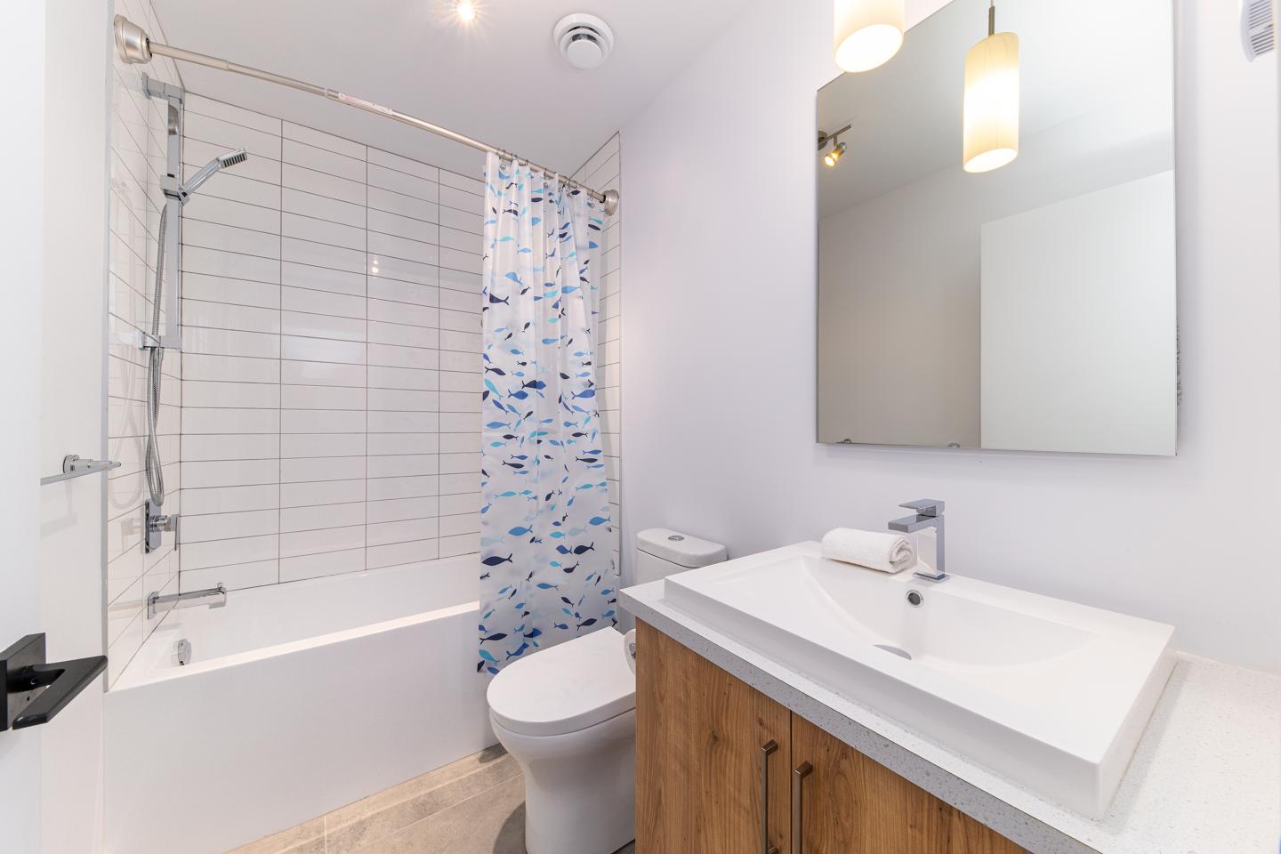 Salle de bain moderne, avec baignoire, lavabo en bois et rideau bleu.