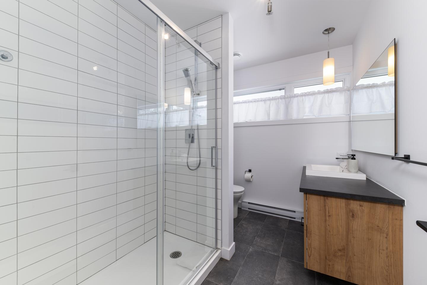 Salle de bain moderne avec douche vitrée, lavabo et carrelage blanc.