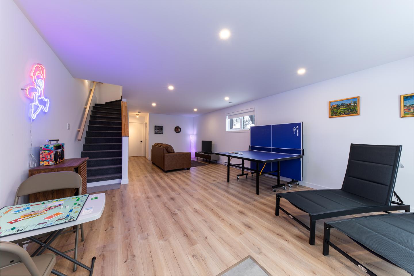 Salle de jeux avec table de ping-pong, canapé, et chaise longue, éclairage violet.