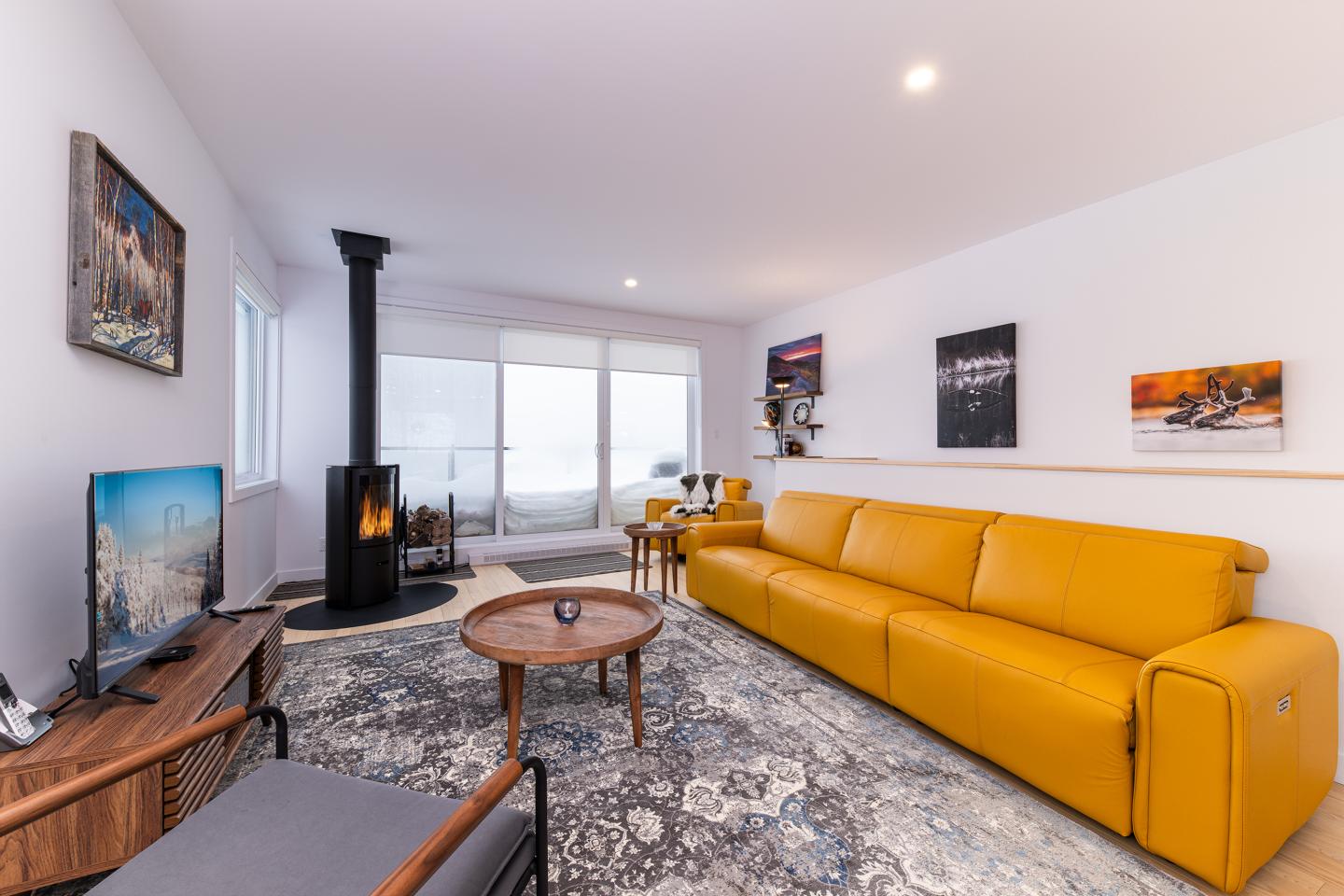 Salon moderne avec canapé jaune, cheminée noire, table basse et tableau sur un mur blanc.