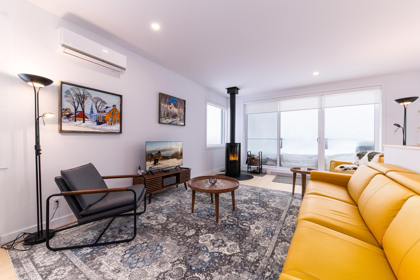 Salon moderne avec canapé jaune, tapis bleu, et poêle à bois.