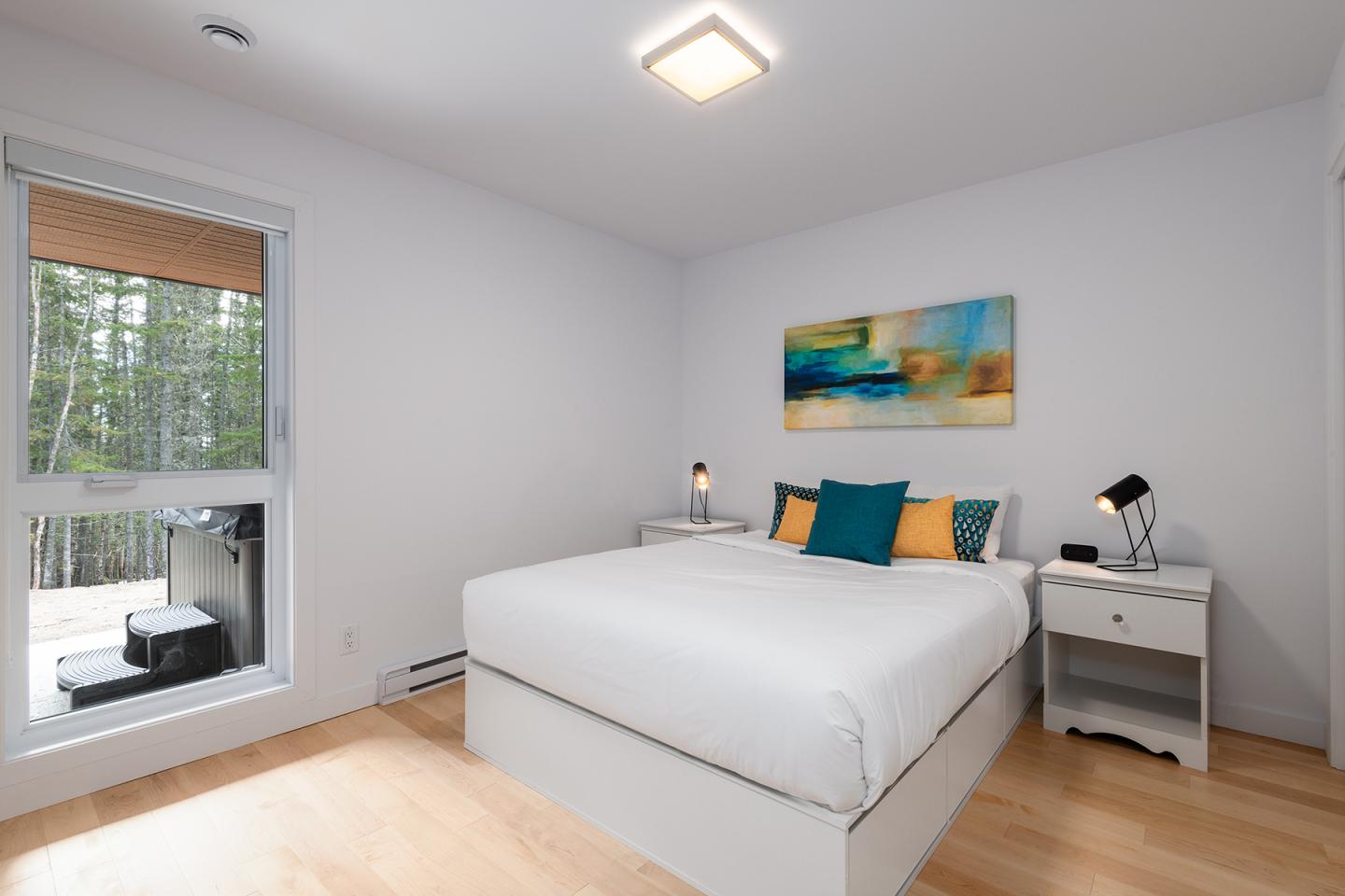 Chambre moderne avec lit double, oreillers colorés, tableau abstrait et fenêtre.