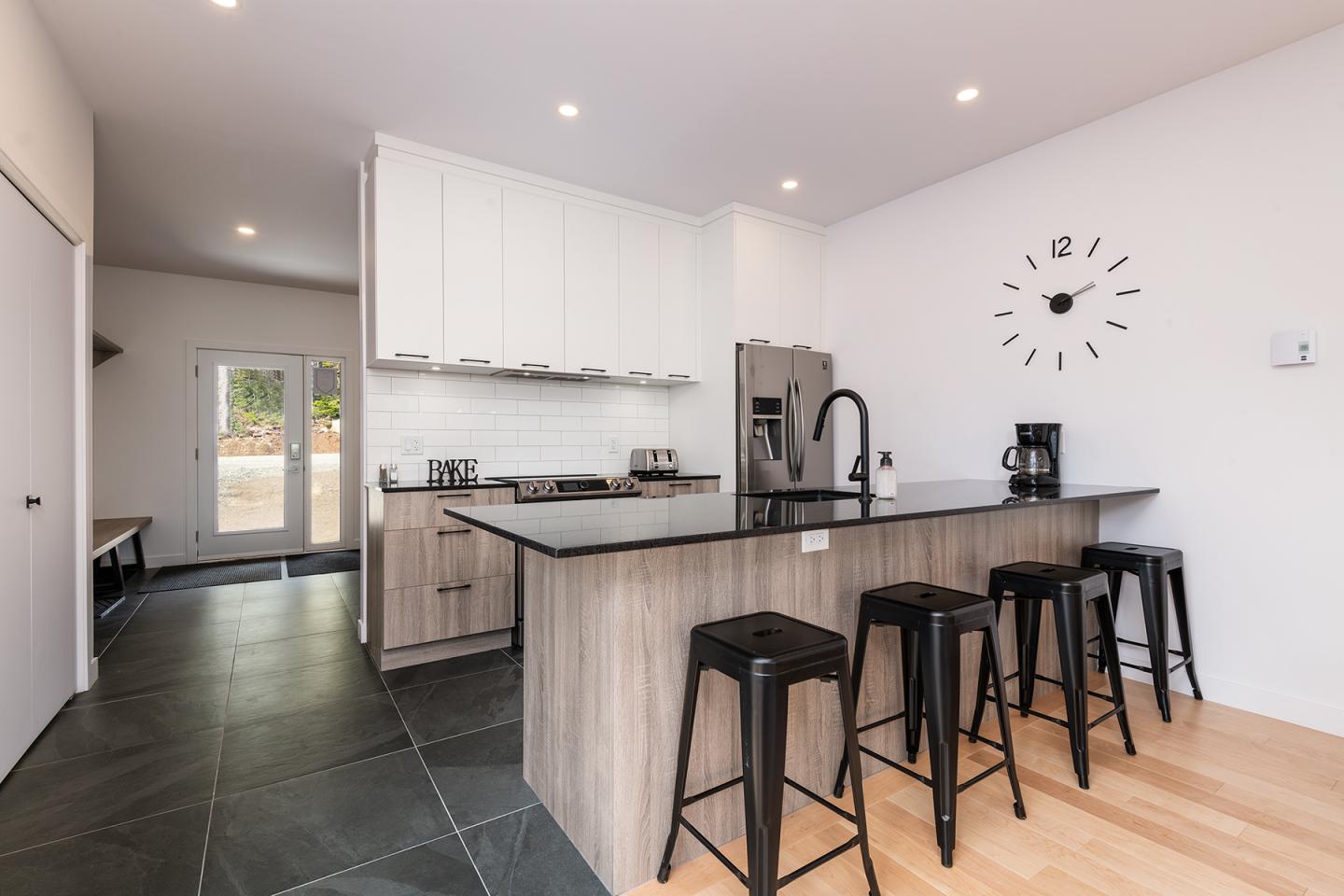 Cuisine moderne avec îlot central, tabourets noirs et horloge murale.
