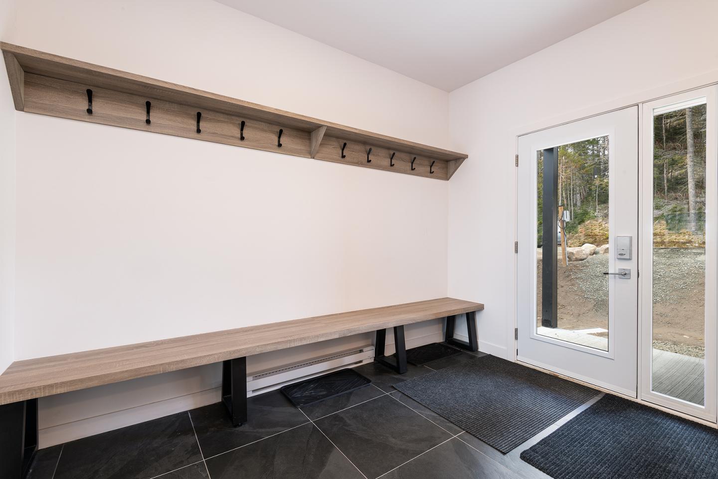 Vestibule lumineux avec banc, crochets et portes vitrées sur jardin.