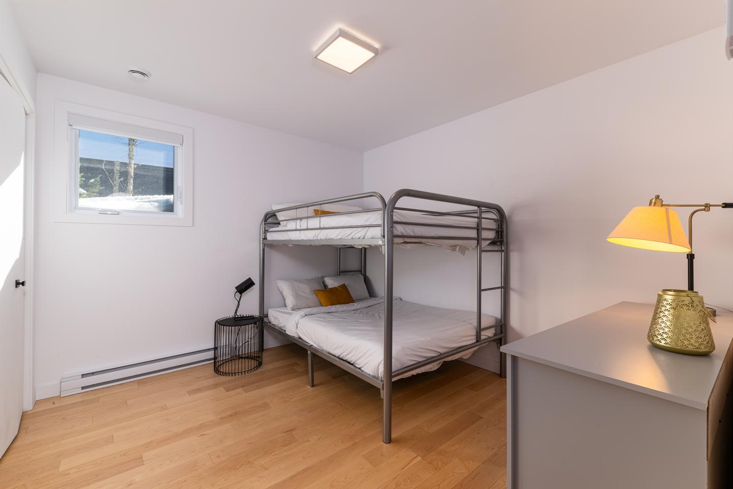 Chambre blanche avec lit superposé, lampe et fenêtre.