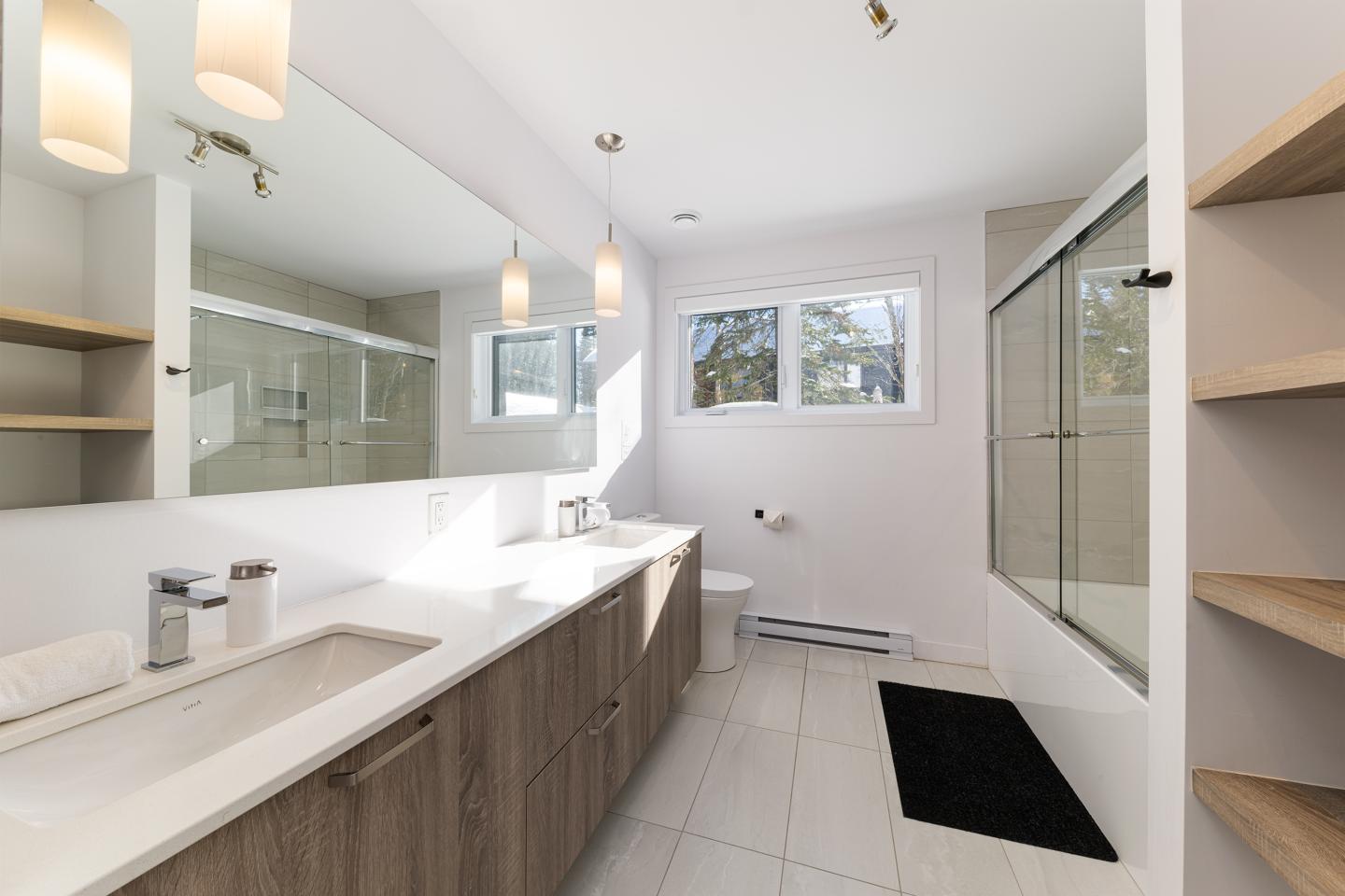Salle de bain moderne, éclairée, avec un grand miroir et douche vitrée.
