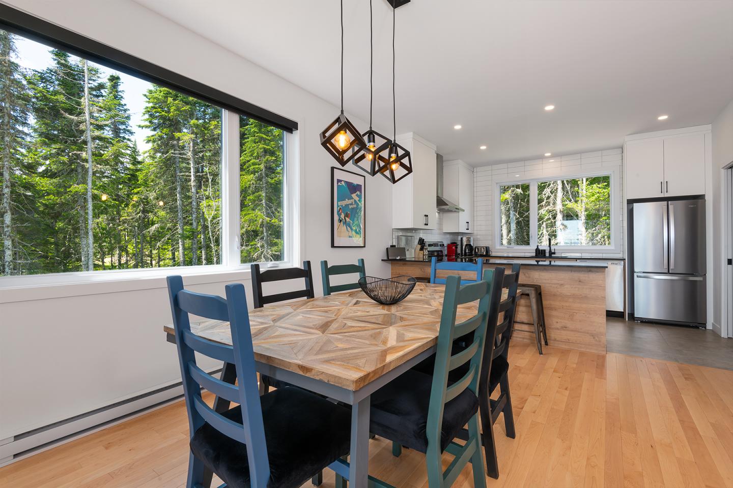 Salle à manger moderne avec grandes fenêtres, table en bois et chaises colorées.
