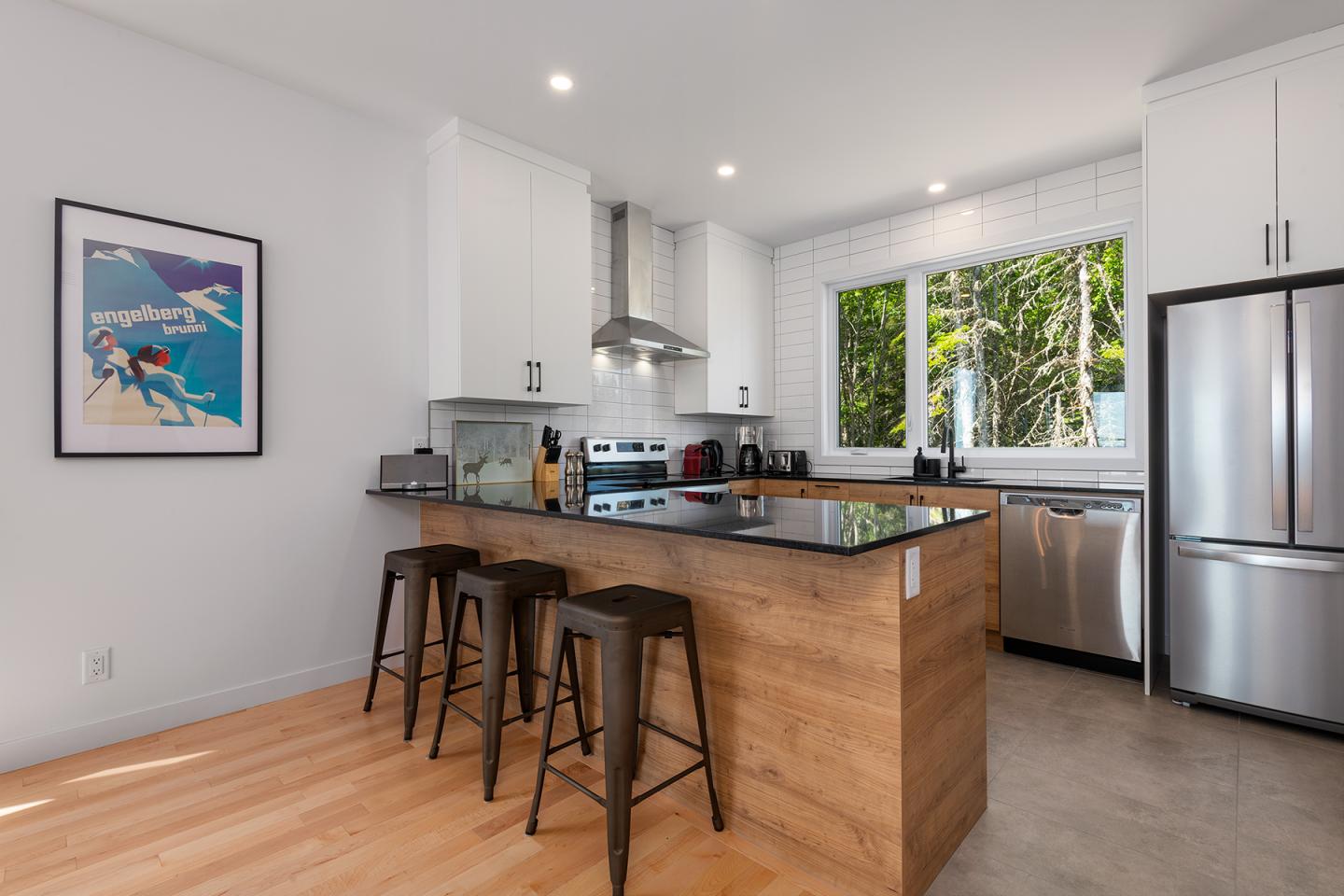 Cuisine moderne avec comptoir en bois, tabourets, et vue sur jardin.
