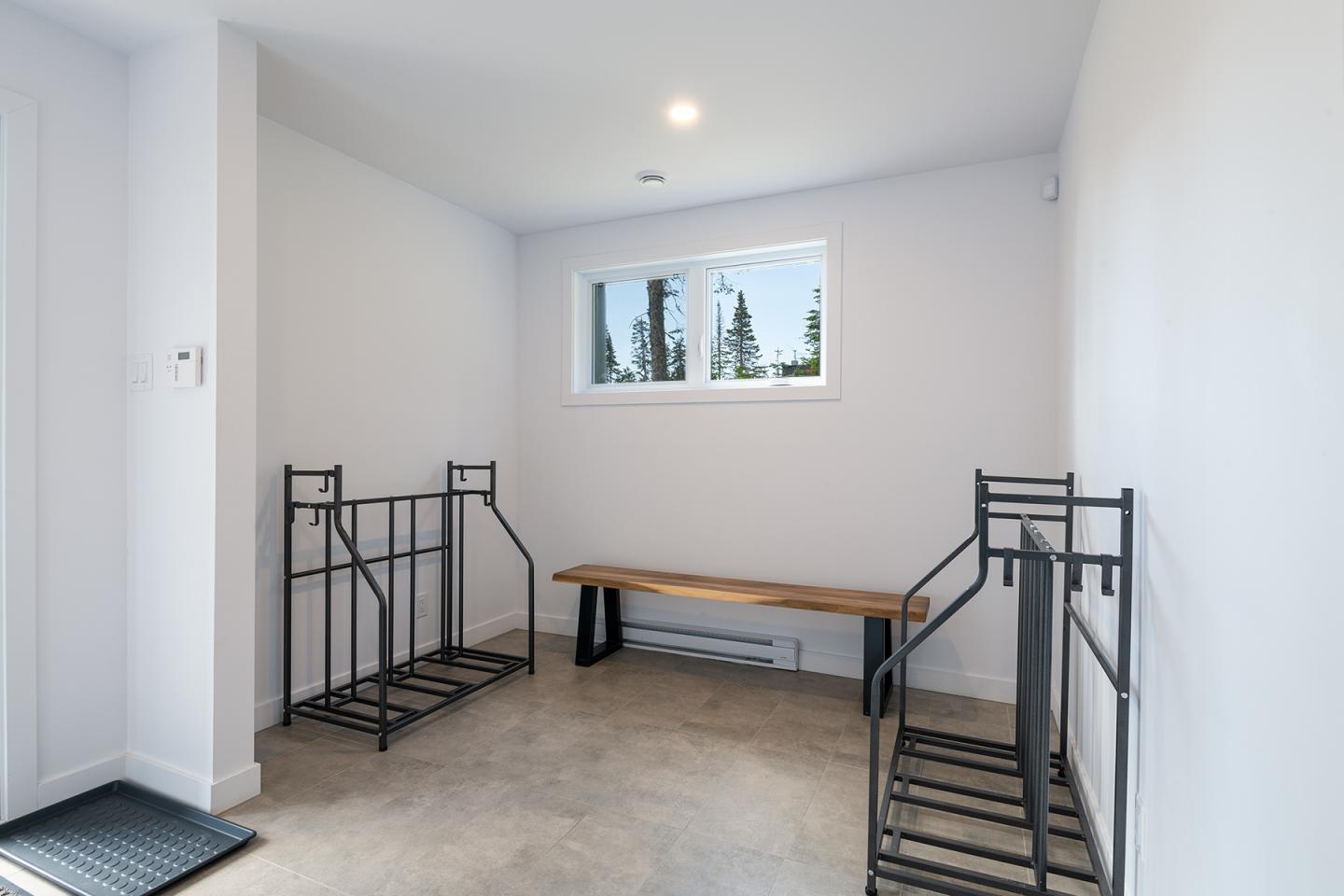 Salle avec sièges en métal et banc, fenêtre donnant sur des arbres.