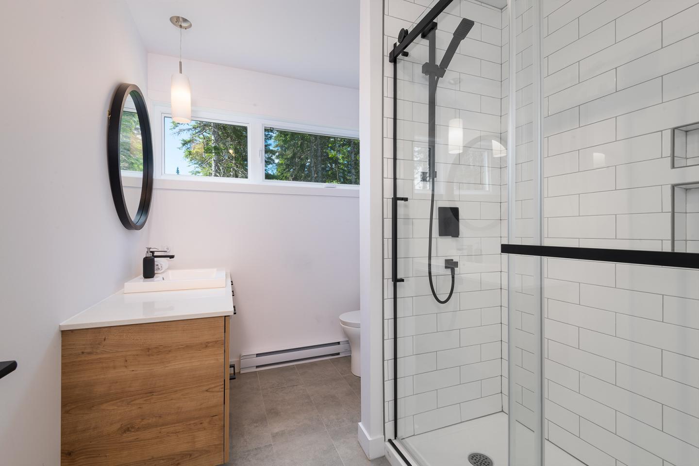 Salle de bain moderne avec douche en verre, lavabo et miroir rond.