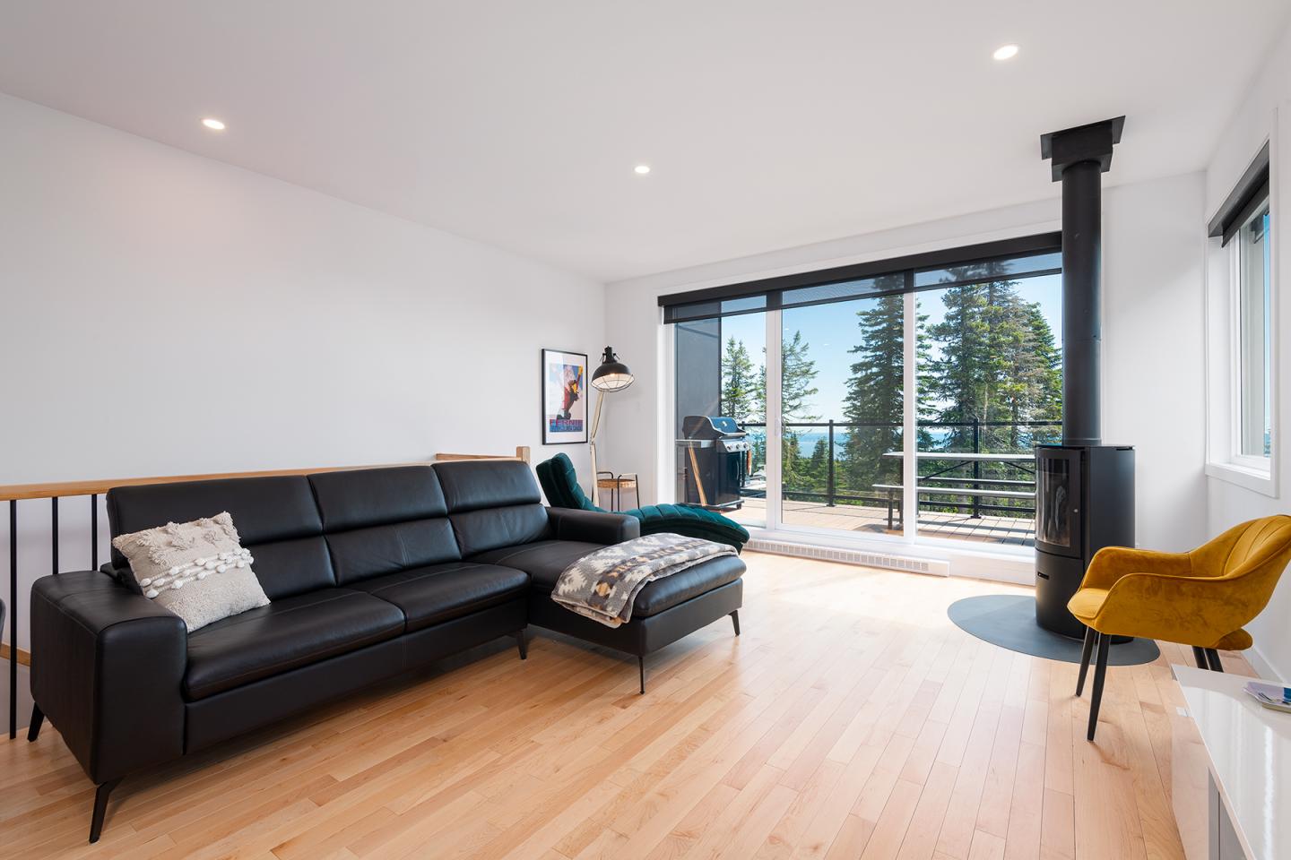 Salon moderne avec canapé noir, baie vitrée et vue sur la nature.