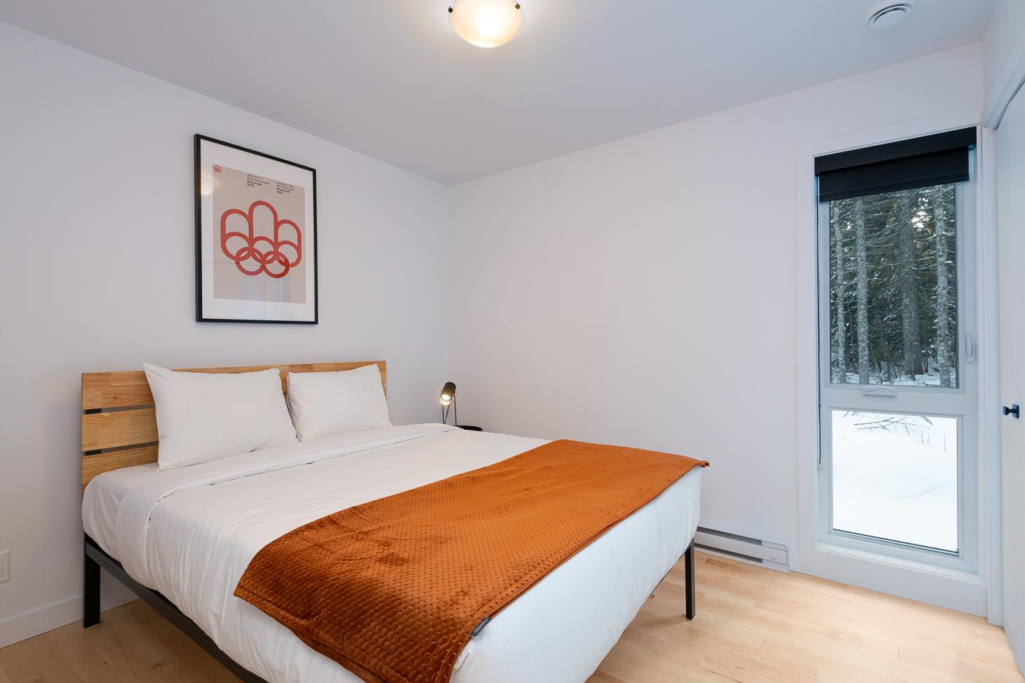 Chambre moderne avec lit double, plaid orange, et une fenêtre donnant sur la neige.