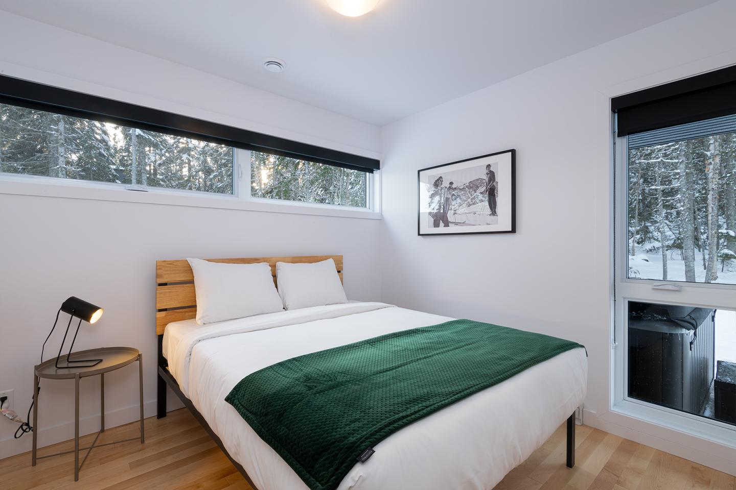 Chambre moderne avec lit double, couverture verte et grandes fenêtres.