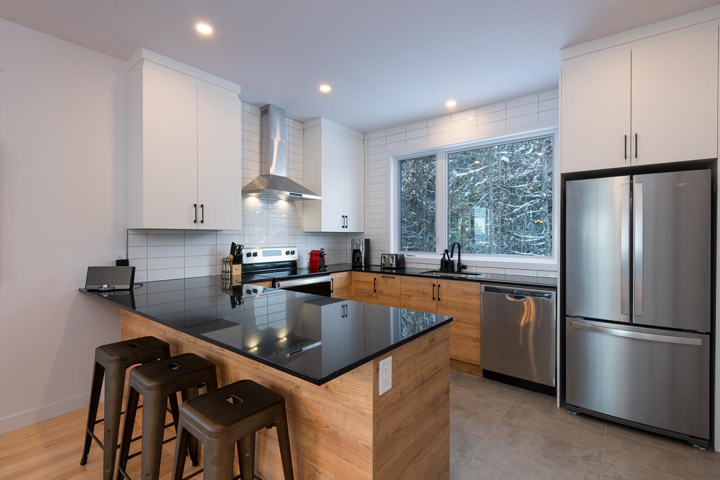 Cuisine moderne avec îlot central, tabourets, et appareils en acier inoxydable.