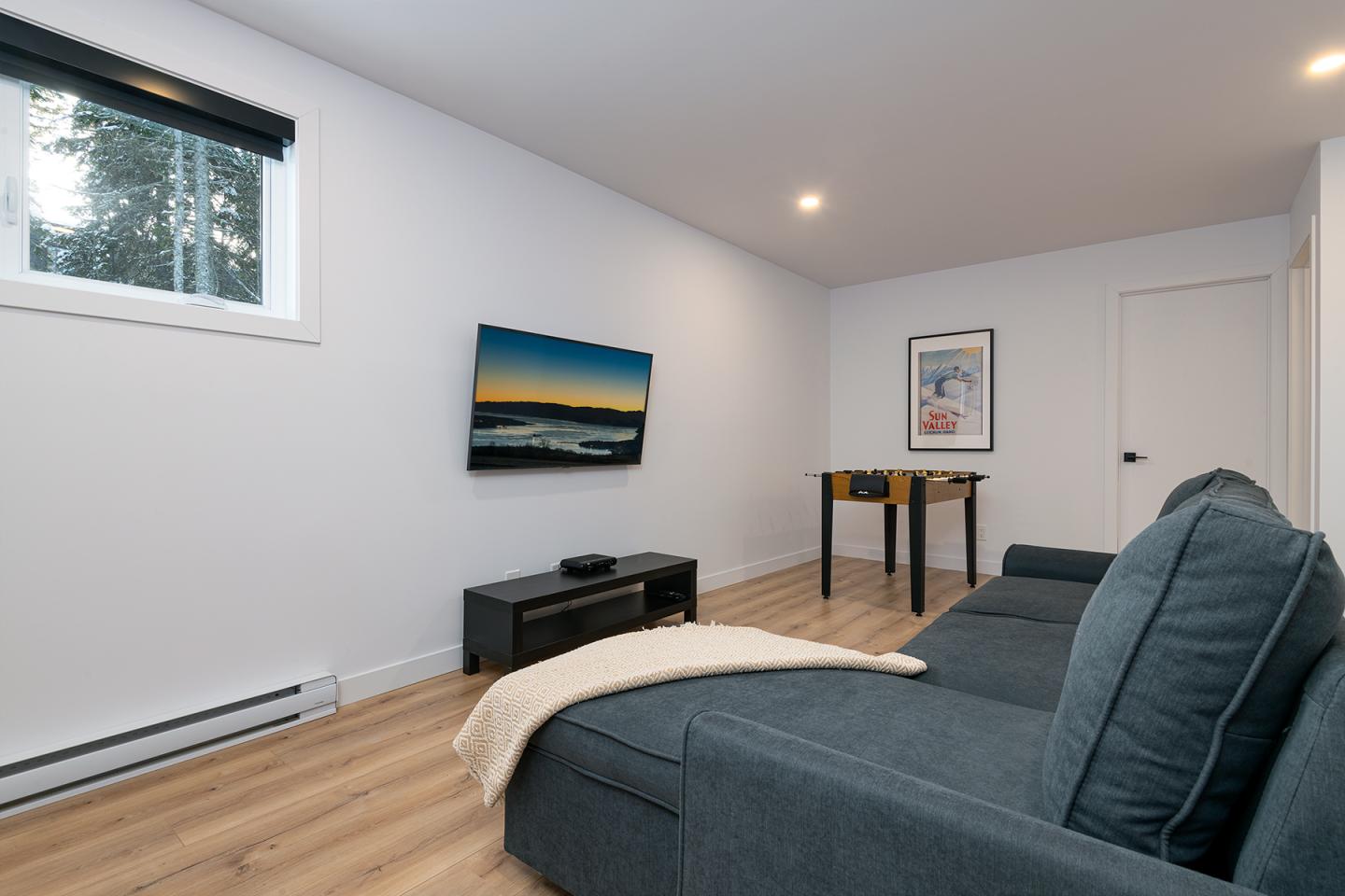Salon moderne avec canapé gris, télé au mur et fenêtre.