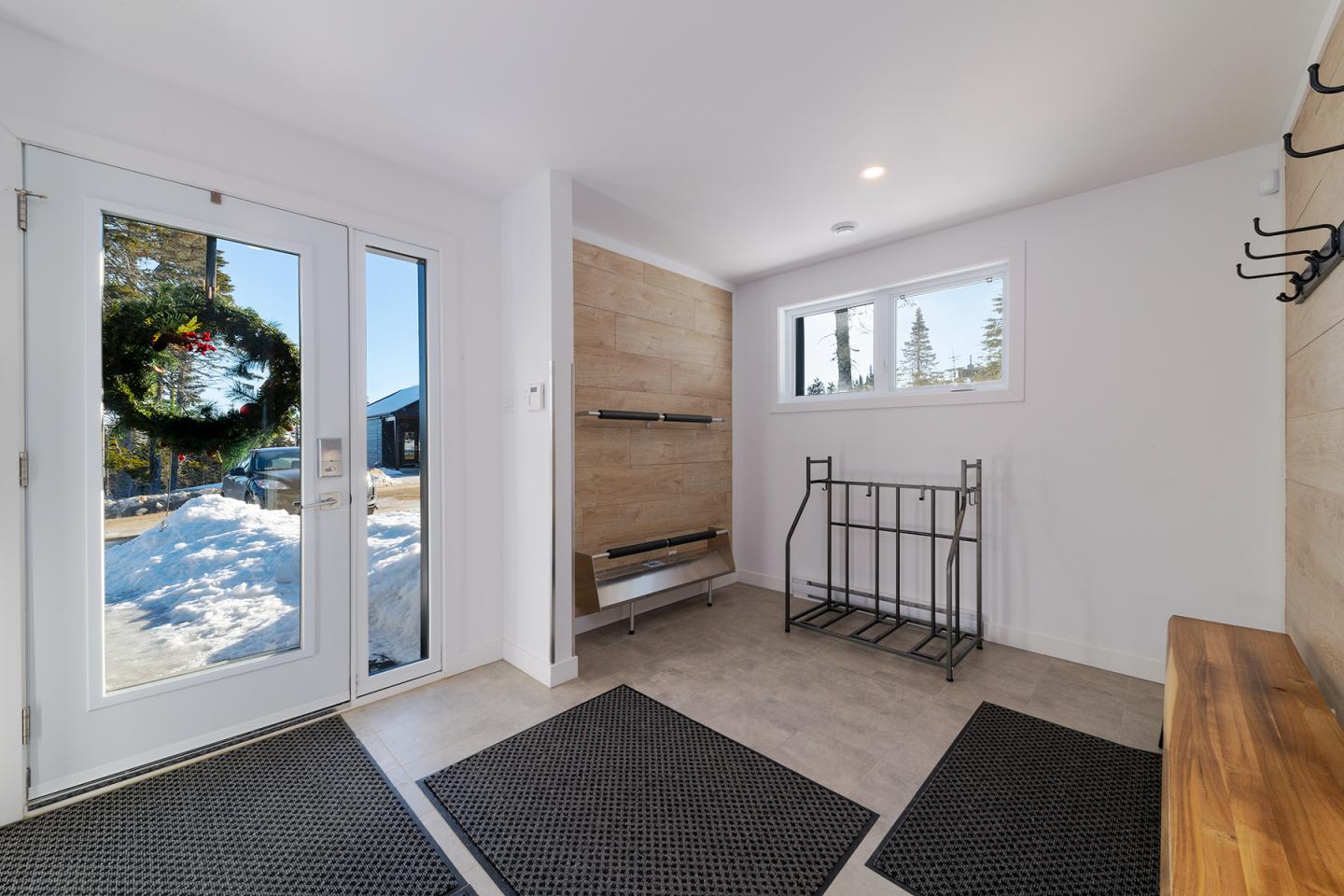Entrée lumineuse avec tapis, porte vitrée et couronne, vue sur l'extérieur neigeux.