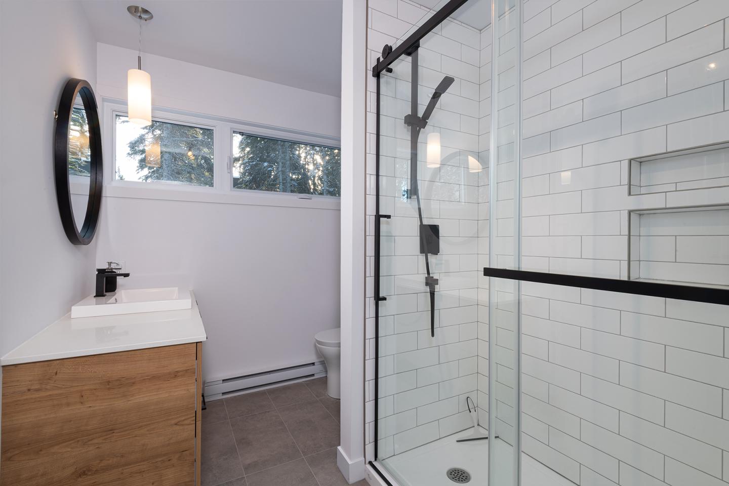 Salle de bain moderne avec douche en verre, lavabo en bois, et miroir rond.