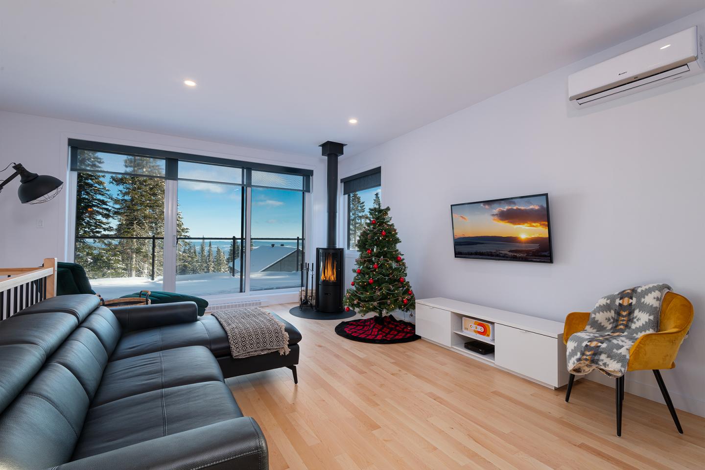 Salon moderne avec sapin de Noël, canapé noir, cheminée et vue panoramique.