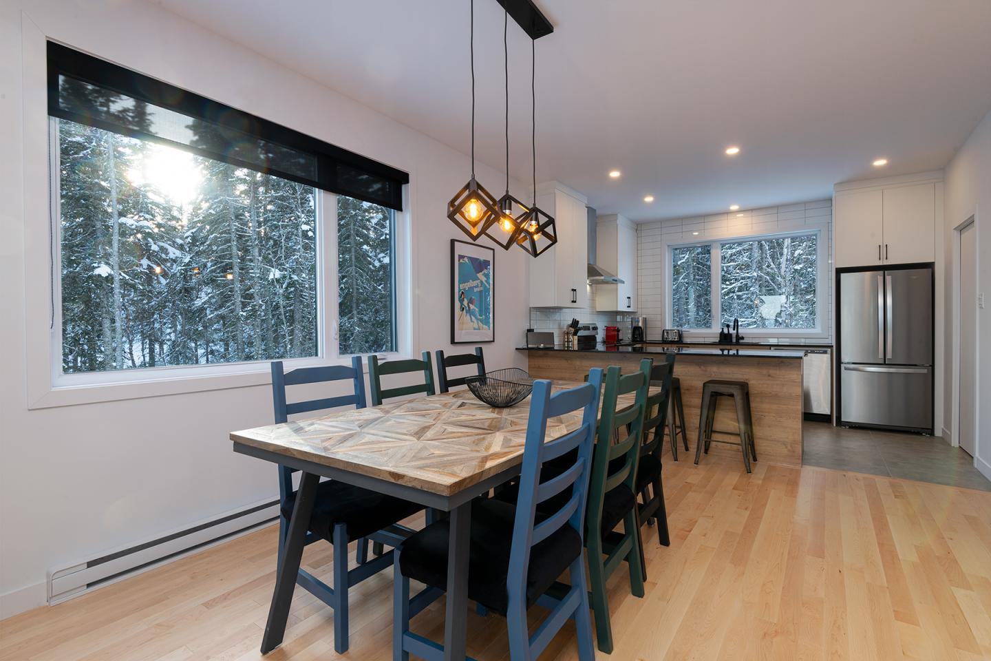 Salle à manger moderne avec table en bois, chaises bleues, et cuisine au fond.
