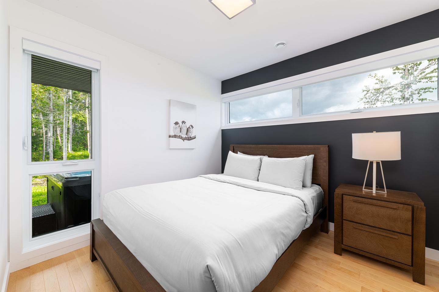 Chambre moderne avec lit blanc, grande fenêtre, lampe sur table en bois.