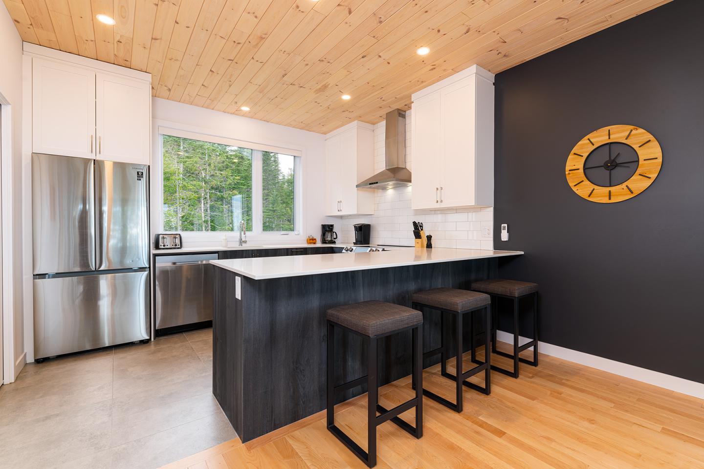 Cuisine moderne avec îlot central, chaises noires et grande horloge murale.
