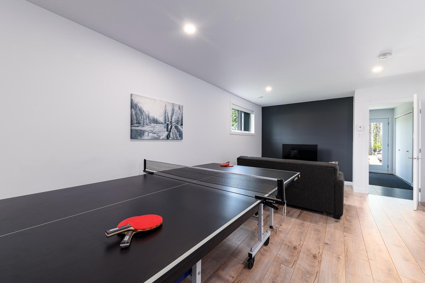 Salle de jeux avec table de ping-pong et canapé sur parquet clair.