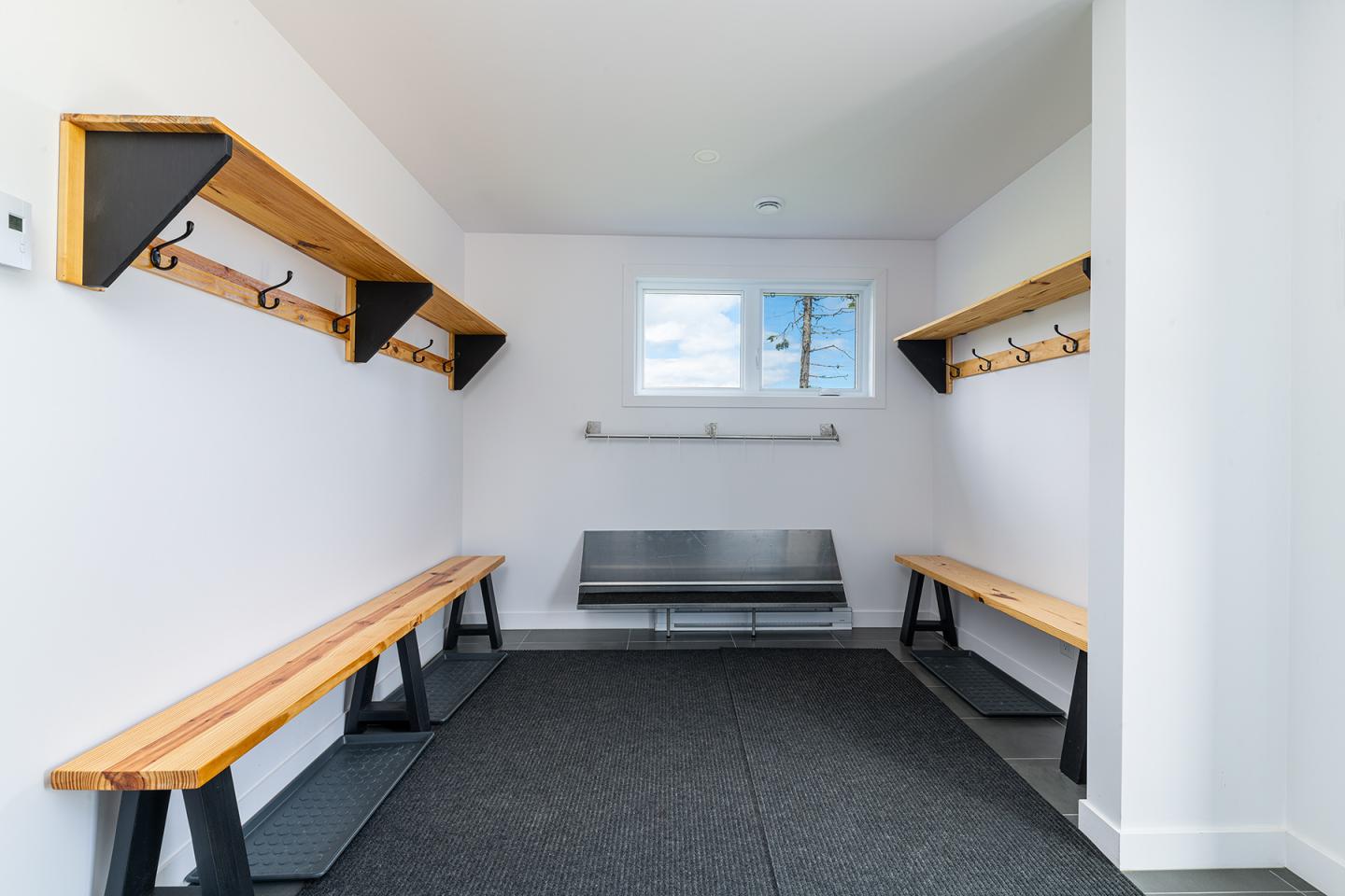 Vestiaire moderne avec bancs en bois et crochets muraux.