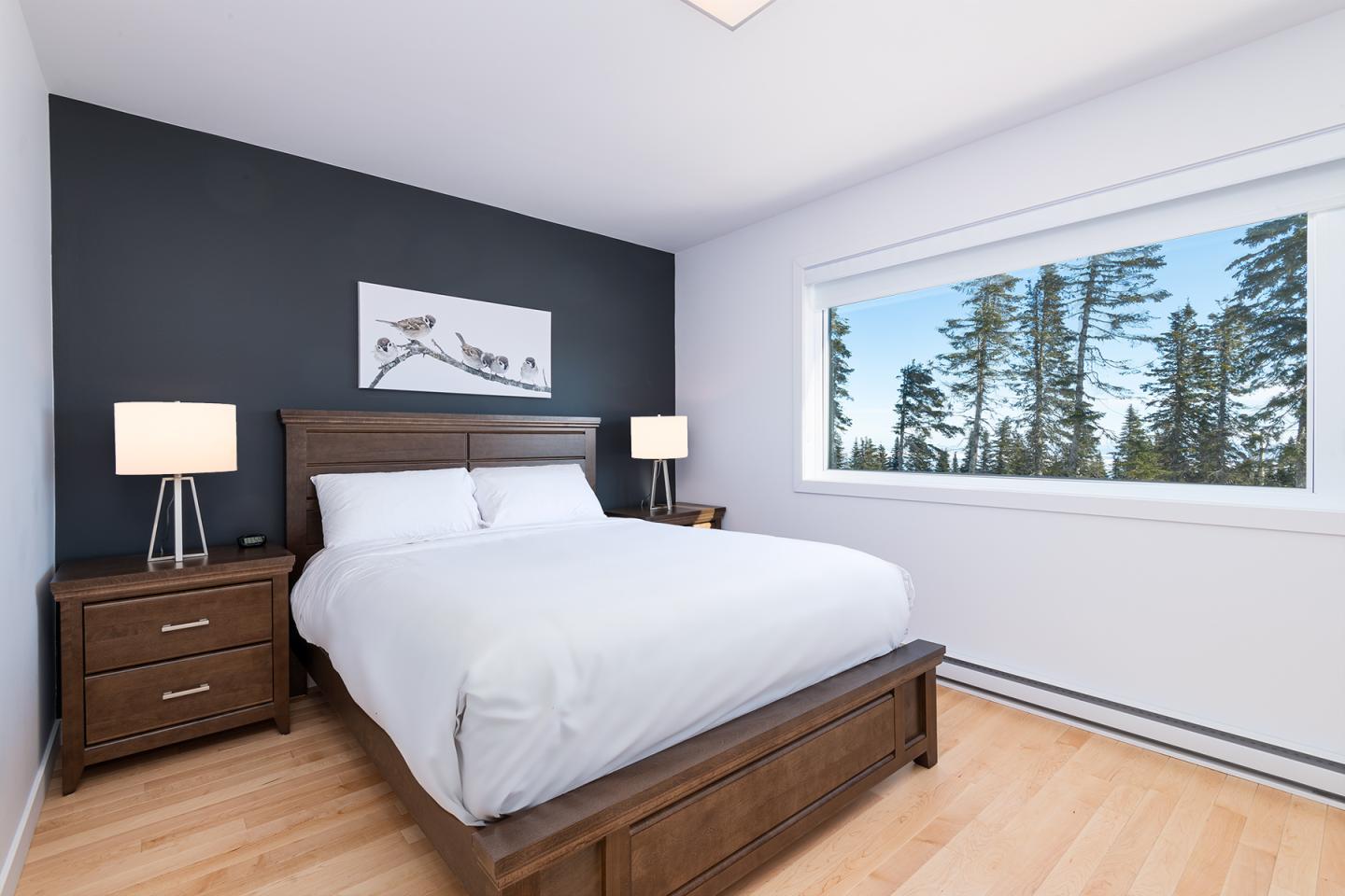 Chambre moderne avec lit double, deux lampes et vue sur forêt par la fenêtre.