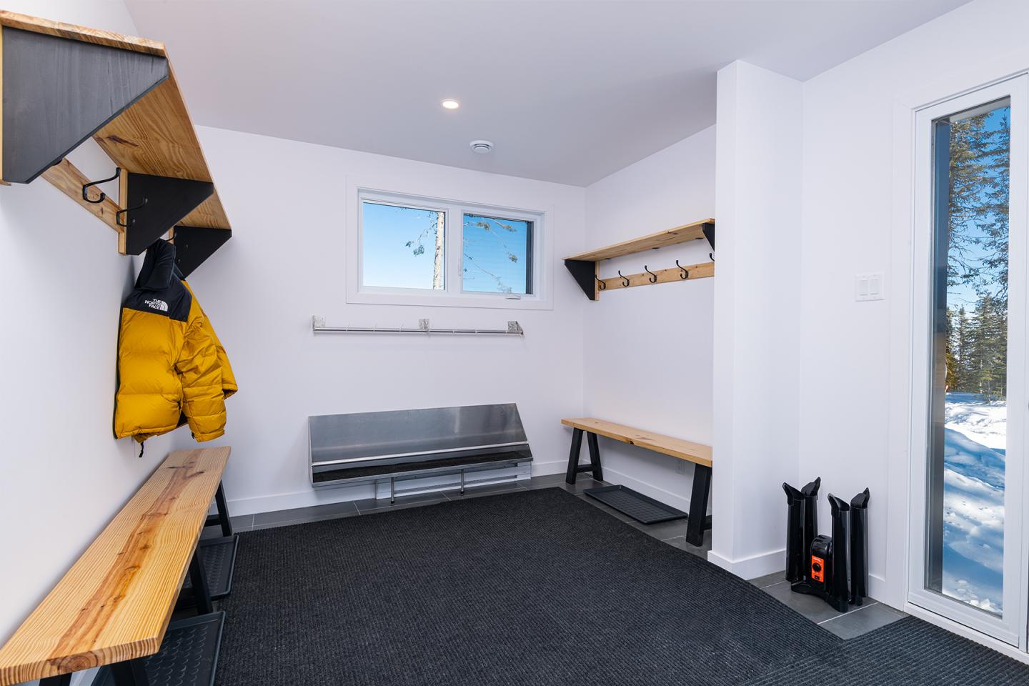 Vestiaire avec bancs en bois, manteau jaune accroché, fenêtre enneigée.