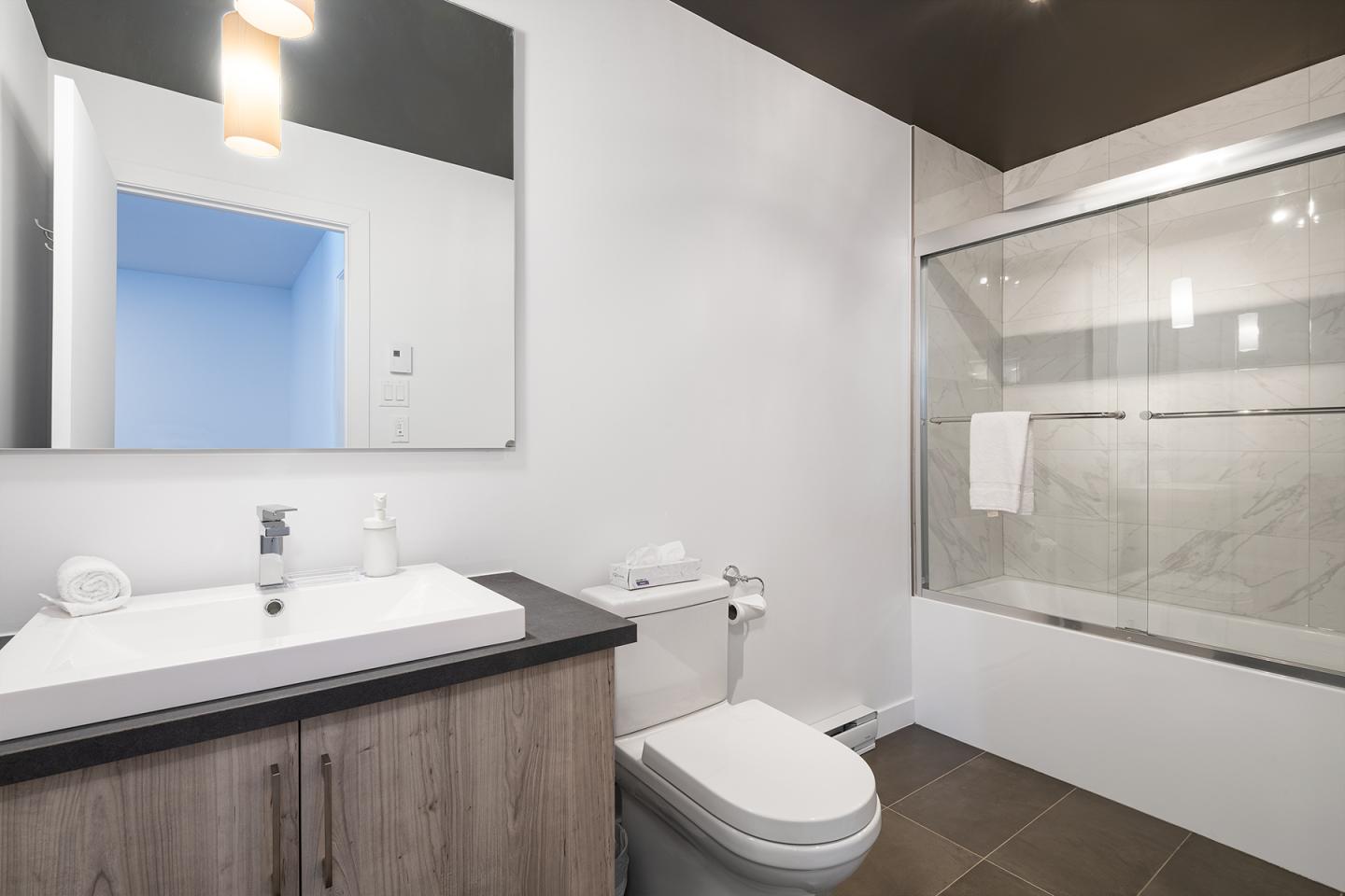 Salle de bains moderne avec lavabo, miroir et baignoire vitrée.