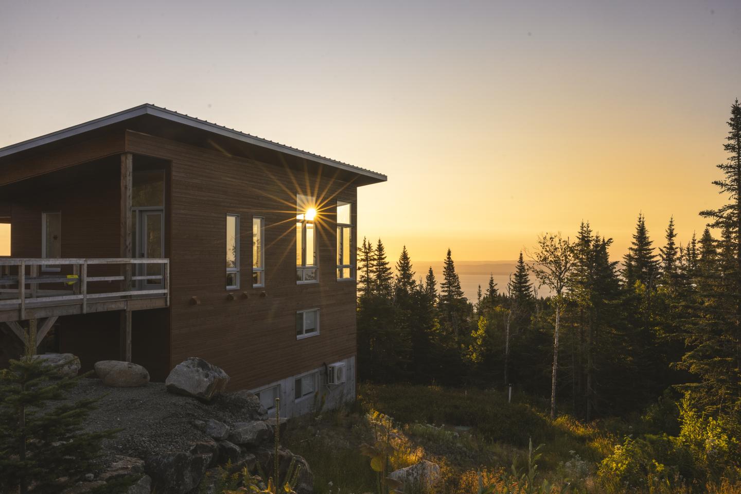 Maison en bois au coucher du soleil, entourée de forêt.