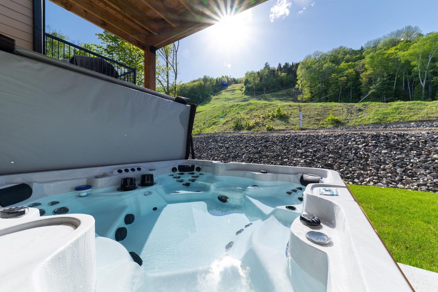 Jacuzzi extérieur ensoleillé avec vue sur colline verdoyante.