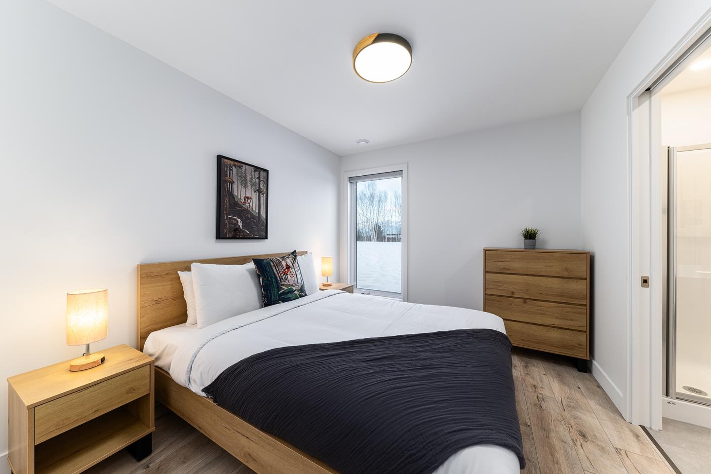 Chambre moderne avec lit double, commode en bois et lampe de chevet.