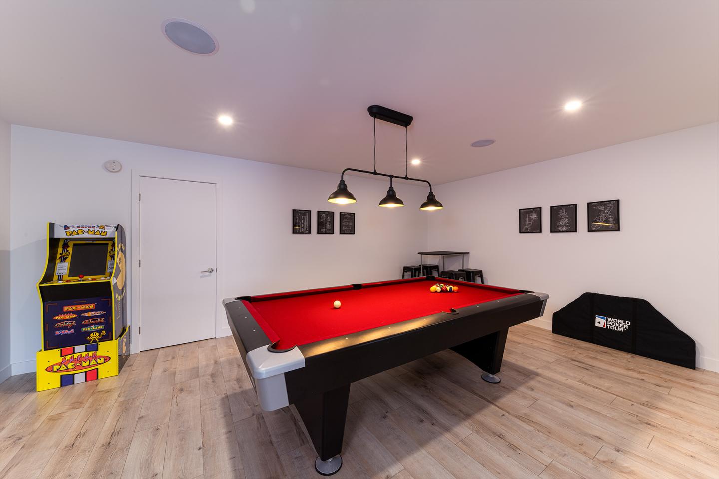 Salle de jeux avec table de billard rouge, borne d'arcade et murs blancs.