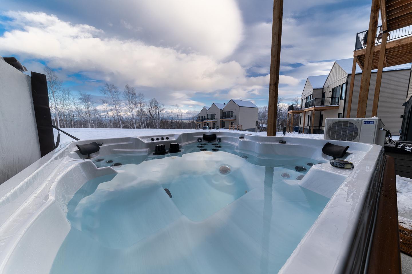Jacuzzi extérieur en hiver avec maisons et montagnes enneigées en arrière-plan.