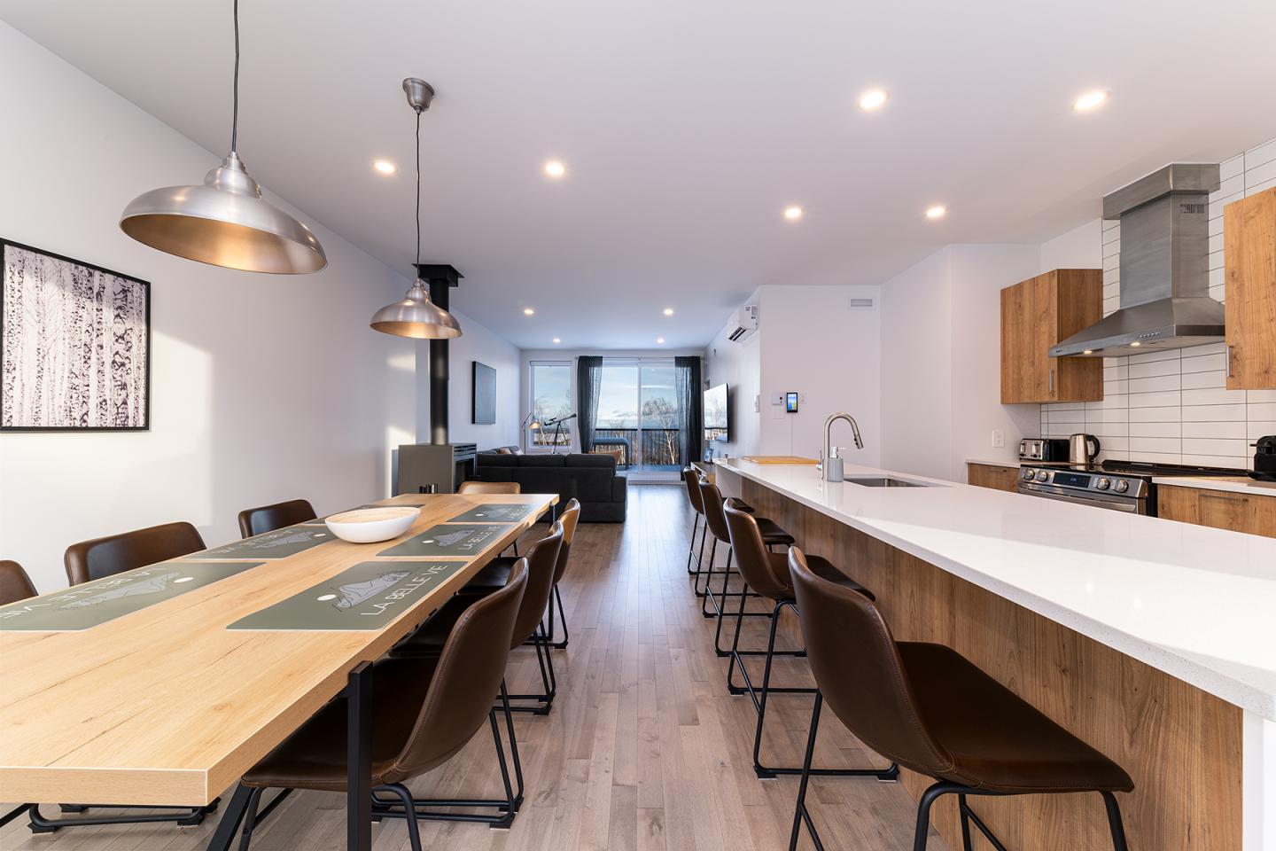 Cuisine moderne avec îlot central et table à manger en bois. Éclairage suspendu.