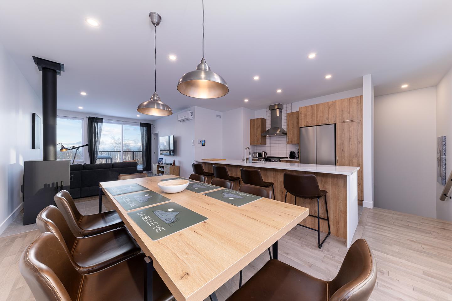 Salle à manger moderne avec table en bois, chaises, et cuisine ouverte.