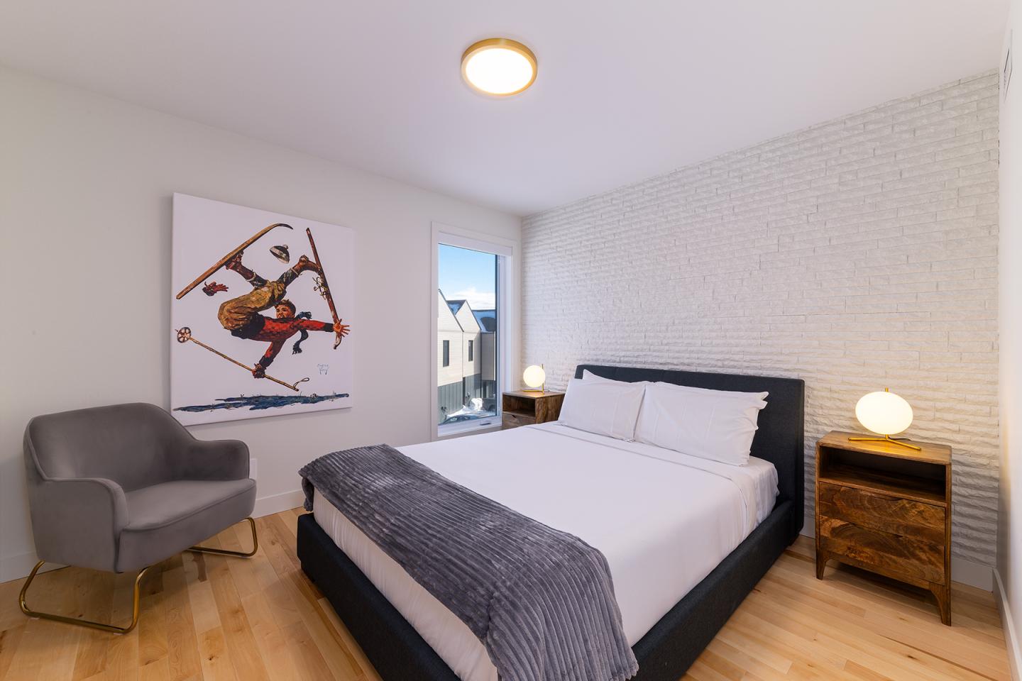 Chambre moderne avec lit double, fauteuil gris et tableau de skieur.