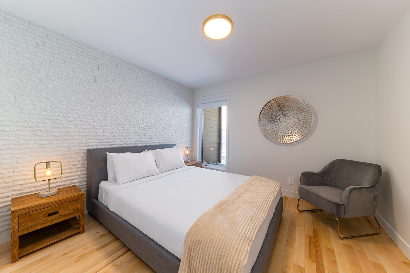 Chambre moderne avec un lit double, chaise grise et décor minimaliste.