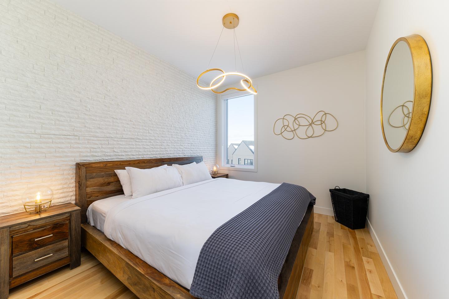 Chambre lumineuse avec lit double, décor minimaliste et lustre moderne.