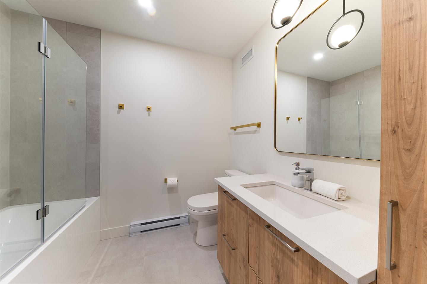 Salle de bain moderne, baignoire, lavabo en bois, miroir rond, éclairage doux.