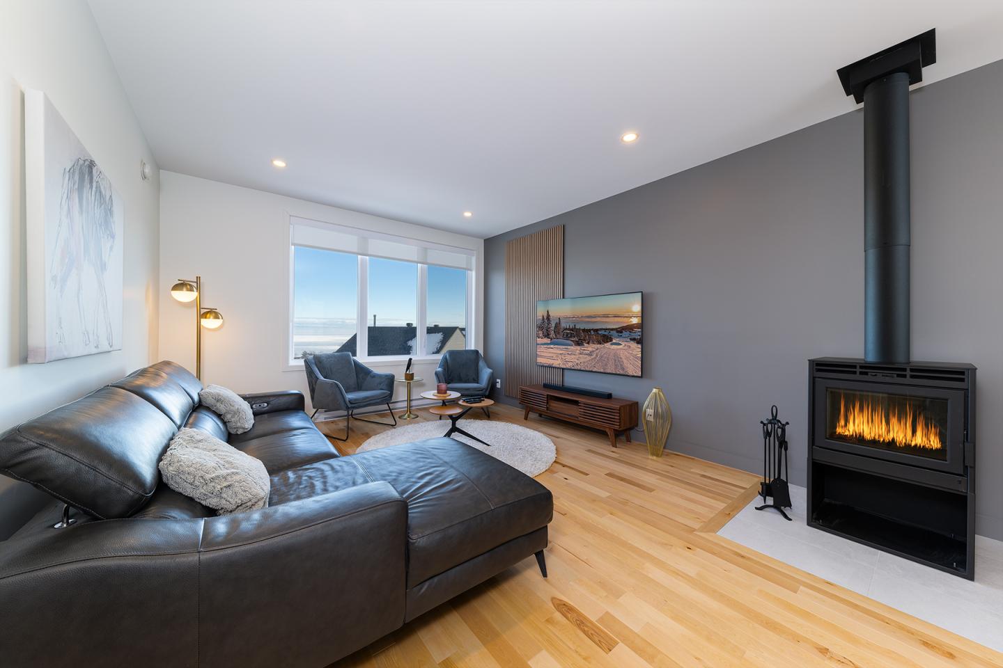 Salon moderne avec canapé en cuir, poêle à bois et vue sur l'extérieur.