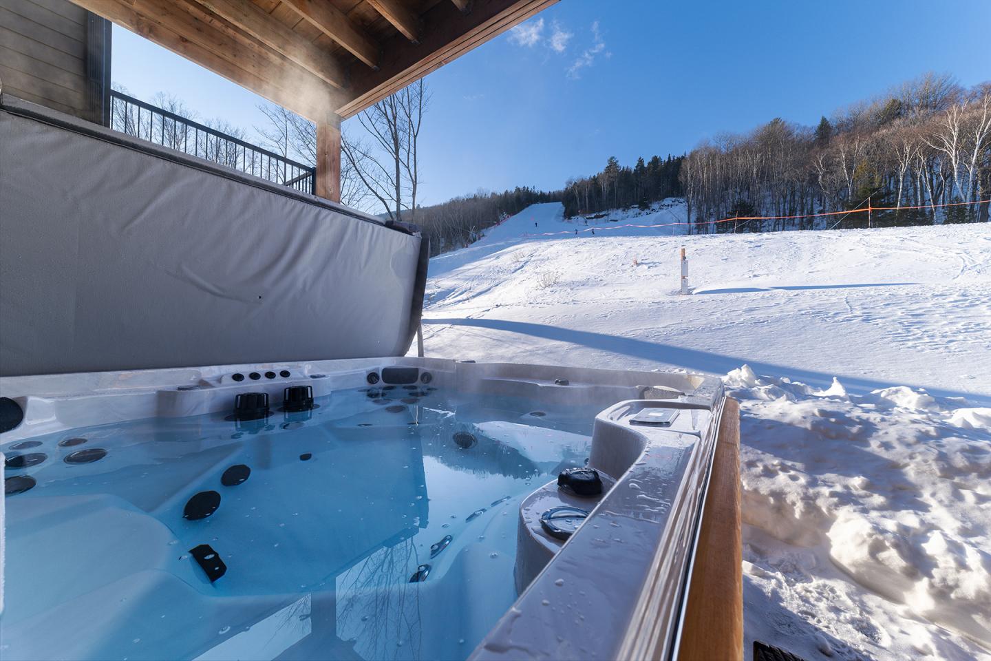 Jacuzzi extérieur fumant avec vue sur paysage enneigé sous ciel bleu.